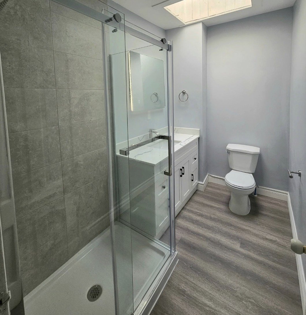 Completed basement bathroom renovation with tiled walk-in shower, quartz vanity and vinyl plank flooring