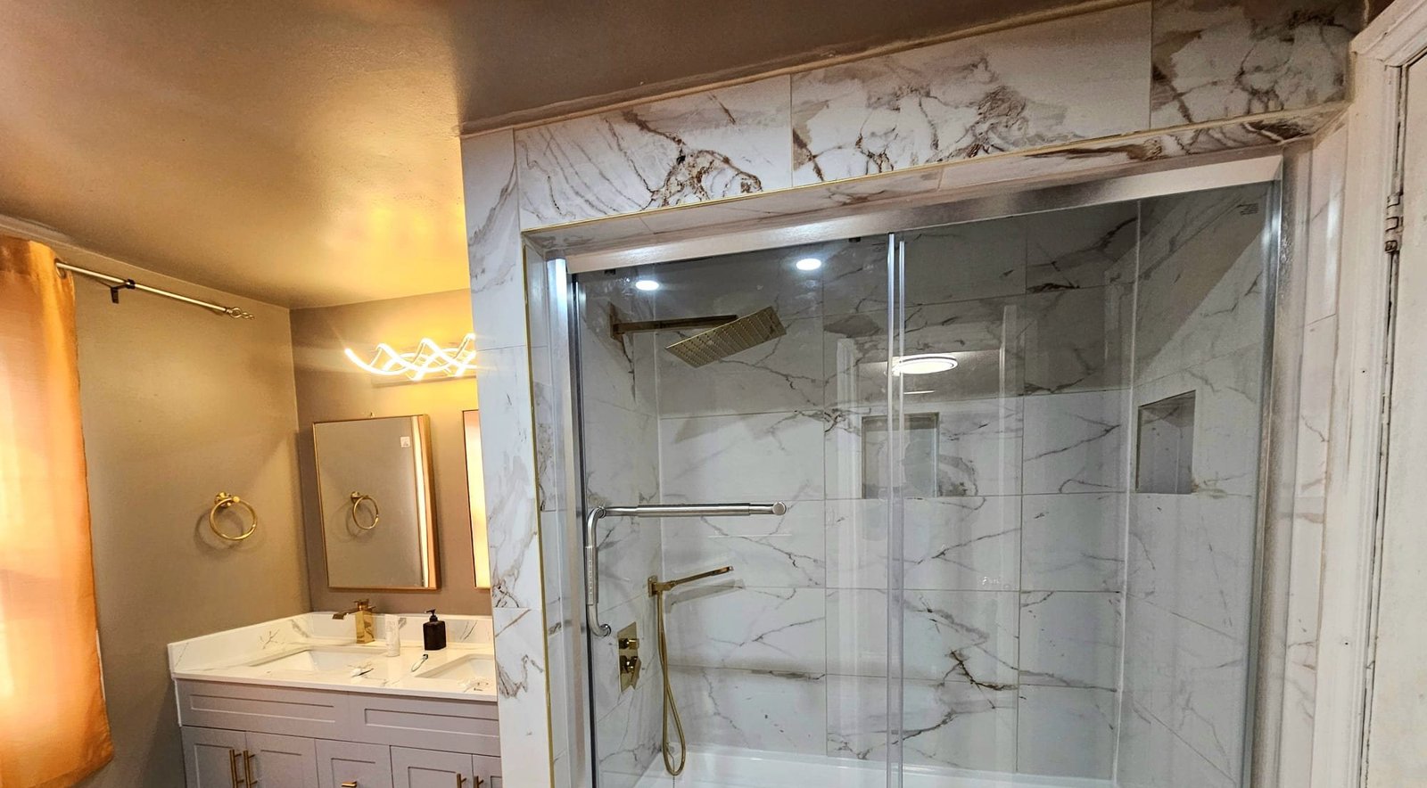 Renovated bathroom with marble tile, glass shower and gold fixtures by Pioneer Plumbing & Home Services in the Greater Toronto Area
